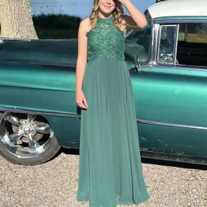 Grön långklänning med spetsdetaljer - grön balklänning med spetsdetaljer på överdelen och en öppen rygg. Klänningen har en flytande kjol och är ärmlös. Den är använd en gång. Det står ingen storlek men passar mig som är  storlek S.