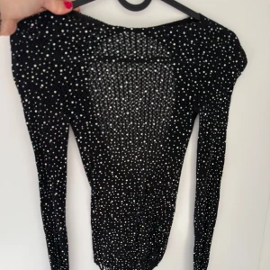 Svart glittrig långärmad topp - Snygg svart långärmad topp med glittriga detaljer. Toppen er en bodystocking. Har blivit använda 1 gång. Storlek: One Size