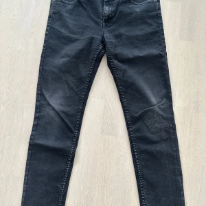 Svarta jeans med korsdetalj från Cheap Monday med chrome hearts patched - Snygga svarta jeans från Cheap Monday med unika korsdetaljer på ena benet. De har en klassisk femficksdesign och en smal passform som ger en modern look. Perfekta för dig som vill ha något extra i garderoben. Med chrome hearts patched work 