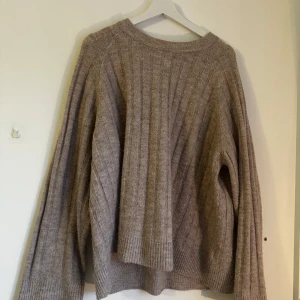 Beige stickad tröja - Säljer en mysig beige stickad tröja med ribbade detaljer. Tröjan har långa ärmar och en avslappnad passform, perfekt för kyligare dagar. Den är både stilren och bekväm.