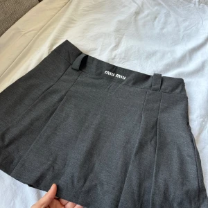 Grå kortkjol från Miu Miu - Snygg grå kortkjol från Miu Miu med en stilren design. Kjolen har en bred linning och är perfekt för en chic look. Den är tillverkad i ett mjukt material som ger en bekväm passform.