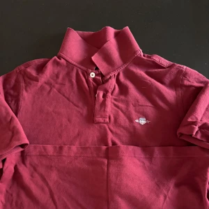 Vinröd pikétröja från GANT - Säljer en snygg vinröd pikétröja från GANT i storlek M. Tröjan har korta ärmar och en klassisk krage med knappar. Perfekt för en stilren look. 💥
