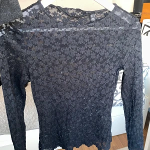 Svart spetsblus - Säljer en elegant svart spetsblus med långärmad design. Blusen har ett vackert blommönster och är perfekt för att lägga till en touch av stil till din garderob. Den är tillverkad i ett lätt och luftigt material. Obs. Att den är sönder i sömnen längst upp bak på tröjan 