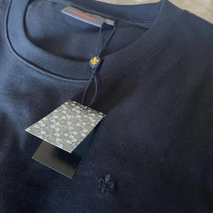 Morris T shirt - Säljer en stilren marin blå t-shirt från Morris med rund halsringning. T-shirten har en diskret broderad detalj framtill och är tillverkad i ett mjukt material. Perfekt för en minimalistisk look. || Aldrig andvänd då jag upplever den som lite stor! || frågor? Hör av dig! 