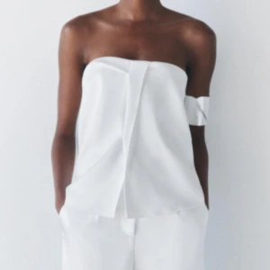 Vit axelbandslös topp - Säljer en stilren vit axelbandslös topp med en elegant veckad design framtill. Slutsåld från Zara, Helt oanvänd med prislapp på! Strl xs 