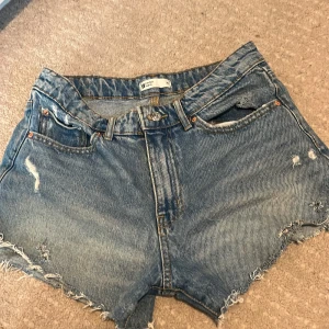 Blå jeansshorts  - Säljer ett par snygga blå jeansshorts från Perfect Jeans. De har en avslappnad look med fransiga kanter och slitningar för en cool stil. Perfekta för sommardagar!
