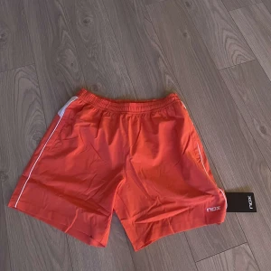 Orange träningsshorts från NOX - orange träningsshorts från NOX med vita detaljer längs sidorna. Perfekta för sport och aktivitet. Elastisk midja för bekväm passform. Gillar inte färgen. 