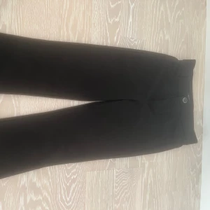 Svarta kostymbyxor/leggings från Zara - Snygga svarta kostymbyxor/leggings från Zara med en stilren design. Byxorna har en knappdetalj i midjan och är perfekta för en elegant look. Dem är utsvängda där nere i benen! De är tillverkade i ett bekvämt material som ger en bra passform.