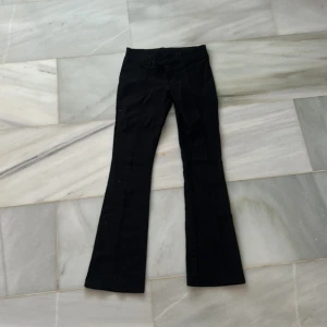 Svarta byxor från H&M - Snygga svarta kostymbyxor från H&M med bootcut-stil. De har en låg midja och stängs med två knappar framtill. Nypris 299kr