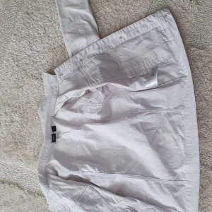 Vit jeansjacka från vero moda, storlek 38 - Snygg vit jeansjacka från vero moda med klassisk krage, knappar framtill och två bröstfickor med lock. Jackan är tillverkad i bomull, polyester och lite elastan för extra komfort. Perfekt att slänga på sig över en klänning eller t-shirt