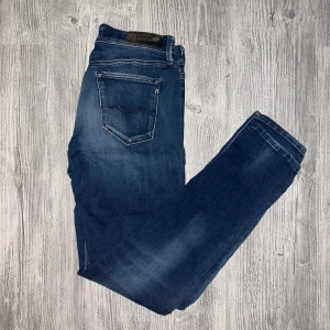 Blå Replay Hyperflex jeans - Snygga blå Replay Hyperflex jeans med klassisk femficksdesign och diskreta slitningar. Jeansen har en normal passform och är tillverkade i stretchigt jeansmaterial för extra komfort. Perfekta för dig som vill ha både stil och rörelsefrihet.