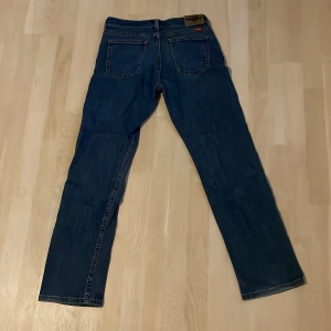 Wrangler Classic Straight jeans blå - Säljer ett par Wrangler Classic Straight jeans i mörkblå denim. Klassisk rak passform med fem fickor och snygga kontrastsömmar. Perfekta för dig som gillar en tidlös look och vill ha jeans som sitter skönt hela dagen.