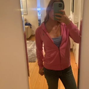 Rosa hoodie från Polo Ralph Lauren - Säljer en rosa hoodie från Polo Ralph Lauren med dragkedja och huva. Det står att den är XL men jag skulle säga att den passar mig som är XS-S om inte lite lite mindre. Tröjan har långa ärmar, känguruficka framtill och den klassiska broderade loggan på bröstet.  Nypris 1400 säljer för att den är lite för liten