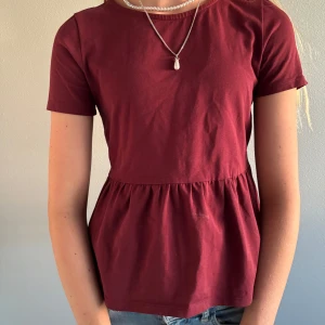 Vinröd T-shirt  - Supersöt vinröd topp med peplumskärning och rund hals. Enkel och stilren design.       T-shirten är från Lindex i storlek 146/152 (barn), men sitter som Xs/S. Perfekt vardagsplagg! Nypris 149 kr – säljer för 90 kr. Endast använd ett fåtal gånger. 😍😍