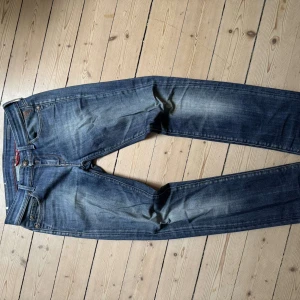 Replay jeans med broderade detaljer - Snygga blå Replay jeans med slitningar och broderade detaljer på fickorna. Jeansen har klassisk femficksmodell, guldfärgade sömmar och ett brunt lädermärke med nitar bak. Perfekt passform och cool faded effekt på låren.