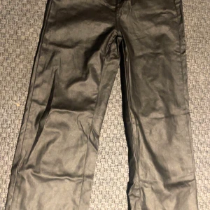 Svarta läderbyxor från SHEIN - Snygga svarta coated byxor från SHEIN i storlek 26. Byxorna har raka ben och en stilren look med bakfickor. Materialet är polyester med en glansig finish som ger en cool vibe. Perfekta för dig som gillar trendiga och stilrena outfits.