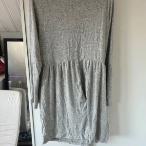 Gråmelerad långärmad klänning - Mysig gråmelerad klänning med lång ärm och avslappnad passform. Klänningen har en rynkad midja som ger en skön och luftig känsla. Materialet är mjukt och stretchigt, perfekt för chill dagar. Enkel design utan synliga detaljer som knappar eller dragkedja.