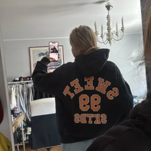 Svart hoodie från Sweet SKTBS - Svart hoodie från Sweet SKTBS i storlek small. Tröjan har huva med snörning, stor ficka framtill och tryck i orange och vitt på ryggen med texten SWEET SKTBS 99. Skön loose passform och tillverkad i mjuk bomull. Köpt på junkyard för cirka 800. Finns ett litet håll på bröstet 