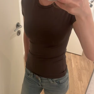 Brun tight t-shirt från Gina Tricot - Snygg brun t-shirt från Gina Tricot i storlek S. Modellen är tight med korta ärmar och rund halsringning. Materialet är mjukt och stretchigt, perfekt för en clean och enkel look. Använt en enstaka gång. 