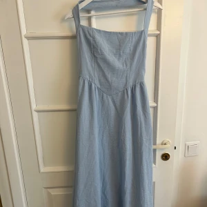 Ljusblå långklänning - Superfin ljusblå långklänning med halter neck. Klänningen har en markerad midja och faller snyggt ner mot anklarna. Perfekt för sommardagar och har en öppen rygg som ger en fräsch känsla.