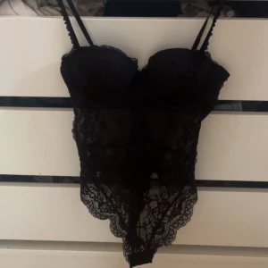 Svart spetsig korsettbody😍 - Säljer en svart korsettbody med tunna axelband och vacker spets över hela plagget. Den har vadderade kupor och fina spetsdetaljer längs kanterna❤️endast använd en gång!