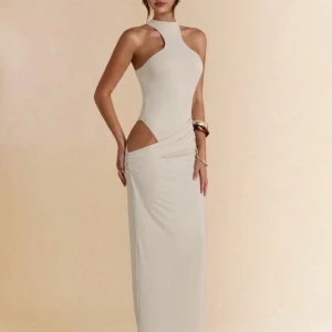 långklänning - Supersnygg beige långklänning med höghalsad design och  cut-out vid höften. Endast använd en gång.