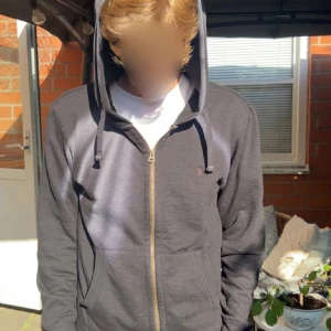 Svart hoodie från Polo Ralph Lauren - Svart hoodie från Polo Ralph Lauren med dragkedja framtill och huva med snörning. Klassisk design med liten broderad logga på bröstet och två fickor. Perfekt för en chill och stilren look. Tillverkad i mjuk bomullsmix för extra komfort.