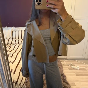 Croppad beige trenchcoat  - Säljer en croppad trenchcoat i beige/ljusbrun förg från Gina Tricot. 