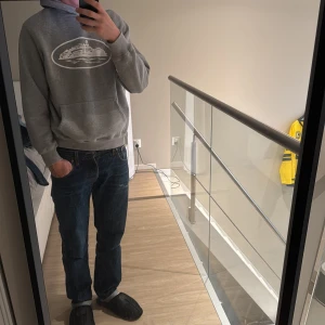 Grå hoodie från corteiz - Grå hoodie med vit tryck av en färja på bröstet. Klassisk känguruficka framtill och mjuk huva. Ribbstickade muddar vid ärmslut och nederkant. Materialet är en skön blandning av bomull och polyester, perfekt för chill dagar. Snygg och enkel design. Passar mig bra, jag är 185cm och väger 75kg✌️