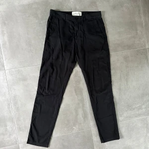 Svarta slim fit chinos A Day's March - Svarta chinos från A Day's March i slim fit-modell. Byxorna är tillverkade i 100% bomull och har klassisk design med snedställda fickor fram och bakfickor med knapp. Perfekta för en clean och stilren look. 1E6