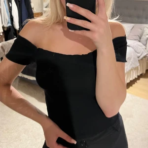 Svart offshoulder topp Gina Tricot XS - Säljer en svart offshoulder topp från Gina Tricot i storlek XS. Toppen är ribbad och har korta ärmar som sitter snyggt över axlarna. Perfekt för dig som gillar en stilren och enkel look med en twist.