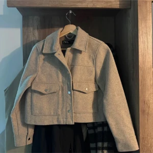 Beige jacka från Zara XS - Snygg beige jacka från Zara i storlek XS. Jackan har klassisk krage, stora bröstfickor med knappar och raka linjer. Perfekt för lager-på-lager och har en stilren, minimalistisk vibe. Materialet känns mjukt och har en ullig look.