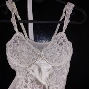 Vit spetsig korsett med satin - Såå vacker gräddvit korsett i spetsdetaljer o liten rosett framtill 