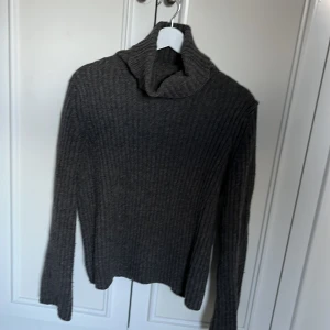 Grå ribbad polotröja från Zara - Mysig grå polotröja från Zara i ribbstickat material. Tröjan har lång ärm och hög polokrage, perfekt för kyliga dagar. Enkel att styla med jeans eller kjol för en chill look.