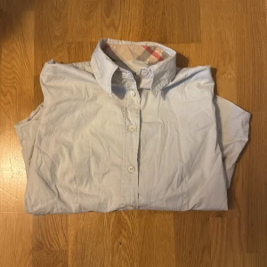 Beige Burberry skjorta XS - Snygg beige skjorta från Burberry i bomull med klassiskt rutigt mönster på insidan av kragen och ärmsluten. Skjortan har knappar framtill och lång ärm, perfekt för en clean och stilren look.