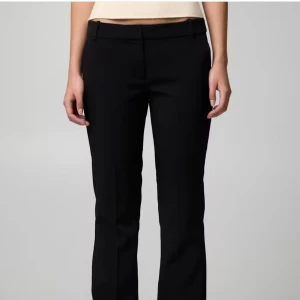 Svarta kostymbyxor med rak passform - Snygga svarta kostymbyxor med klassisk rak passform och midwaist. Byxorna har bälteshällor och stilren design, perfekta för en clean look. Materialet är troligtvis polyester eller bomullsmix för en dressad känsla.