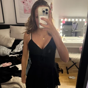 Svart kort klänning  - Supersöt svart kort klänning från New Yorker med tunna axelband som knyts och v-ringning. Klänningen har ett diskret prickigt mönster i tyget och volangig kjol och shorts under💗