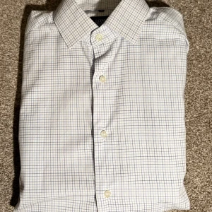 Vit rutig skjorta Long Island slim fit - Vit skjorta från Long Island i slim fit-modell med blått rutmönster. Klassisk krage, knäppning framtill och långa ärmar. Perfekt för dig som gillar en stilren och fräsch look. Skjortan är i bomull och har en modern passform.