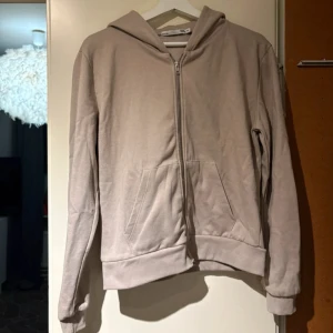 Hoodie - Enkel och stilren beige hoodie från lager 157 med dragkedja framtill och två stora fickor. Tröjan har huva och långa ärmar, perfekt för chill dagar. Tillverkad i mjuk bomullsmix som känns skön mot huden.
