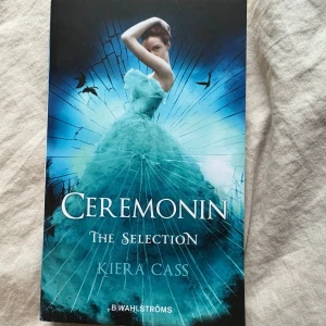 Ceremonin - The Selection - En fängslande bok med en magisk omslagsbild där en ung kvinna i en blå klänning står i centrum. Perfekt för dig som gillar romantik, kungliga intriger och spännande berättelser om att följa sina drömmar. Första delen i succéserien The Selection.