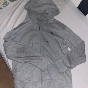 Grå hoodie Polo Ralph Lauren - Snygg grå hoodie från Polo Ralph Lauren med dragkedja och klassisk logga på bröstet.  Perfekt för chill dagar. Den är i bra skick.                     Den är i storlek M men den passar även L den är mer i en L storlek 