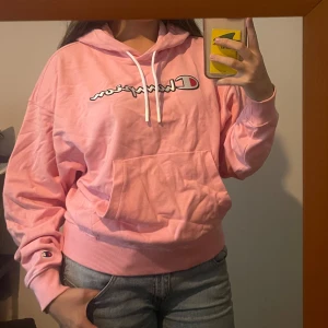 Rosa Champion hoodie med huva - Säljer en rosa hoodie från Champion med vit snörning och stor magficka. Tröjan har en oversized passform, ribbade muddar och logotypen broderad på ärmen. Som du ser är den inte struken, så ser mycket bättre ut när den är😅