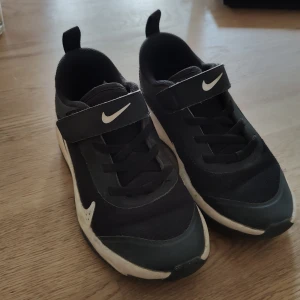 Svarta Nike sneakers med kardborre - Svarta Nike sneakers i mesh och syntet med vit sula och tydliga swoosh-loggor. Skorna har både snörning och kardborreband för enkel påtagning. Storlek 30