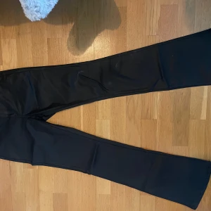 Svarta utsvängda skinnbyxor  - Säljer ett par svarta bootcut-byxor från Vero Moda i storlek S. Byxorna har en snygg utsvängd passform och är tillverkade i ett stretchigt material med polyester, viskos och elastan. Perfekta för dig som gillar en klassisk men trendig look. Medelhöga från vero Moda 