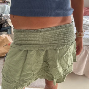 Grön volangkjol - Snygg ljusgrön volangkjol med bred smockad midja och volangig nederdel. Kjolen har en avslappnad passform och är gjord i ett tunt, skönt bomullstyg. Perfekt för varma dagar och enkel att styla med crop tops eller linnen.