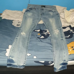 Ljusblå ripped jeans från Purple Brand - Säljer ett par ljusblå jeans från Purple Brand med slitna detaljer på knäna och snygg tvätt. Jeansen har klassisk femficksdesign, smal passform och är tillverkade i bomull. Perfekta för en avslappnad streetstyle-look.