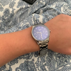 Klocka (Regal) - Stilren klocka från Regal med blå urtavla och tre mindre urtavlor. Armbandet är i blankt silverfärgat metall och har klassisk länkdesign. Klockan har tydliga vita markeringar och en modern, rund form som passar till många olika stilar. Säljer då jag ej använder den längre