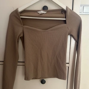 Beige ribbad långärmad topp - Snygg beige långärmad topp med ribbad struktur och söt sweetheart-urringning. Toppen har en figurnära passform och är perfekt att styla med jeans eller kjol för en trendig look.