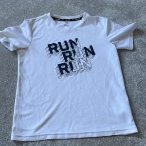 Vit sportig t-shirt från H&M - Vit t-shirt från H&M Sport med trycket 'RUN RUN RUN' i mörkblått framtill. Klassisk rund hals och korta ärmar. Tillverkad i lätt och ventilerande polyester, perfekt för träning eller aktiva dagar.