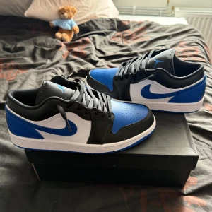 Nike Air Jordan 1 Low, royal toe - Snygga Nike Air Jordan 1 Low (royal toe) sneakers i blått, svart och vitt skinn. Klassisk siluett med perforerad tå, svart snörning och vit mellansula. Blå yttersula och ikoniska swoosh-loggan på sidorna. Perfekta för dig som vill sticka ut med stil. Storlek 45, endast använda 3-4 gånger! Box ingår!